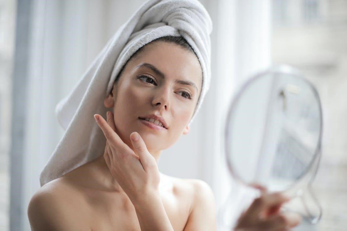Image of a woman with a white towel wrapped on her head looking in a mirror
